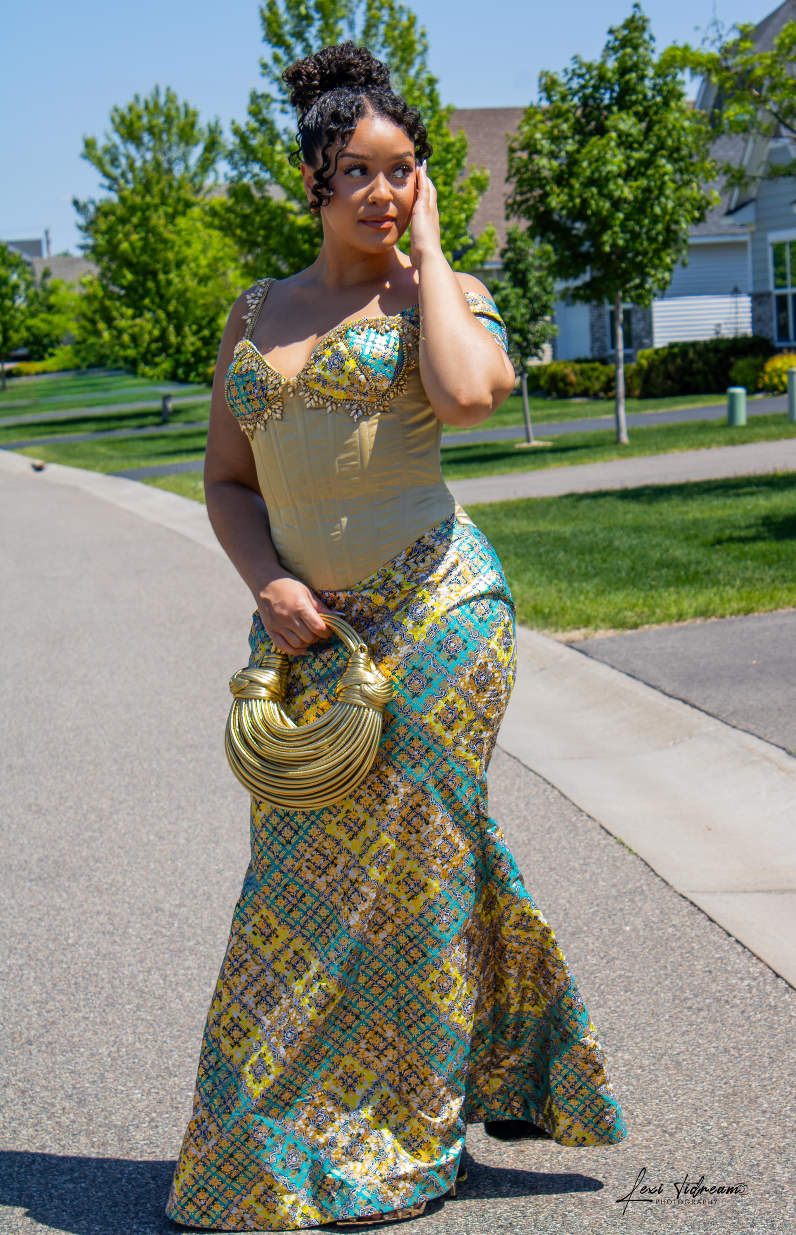 Woman in a gold and teal cultural fashion gown with sculptural gold handbag
