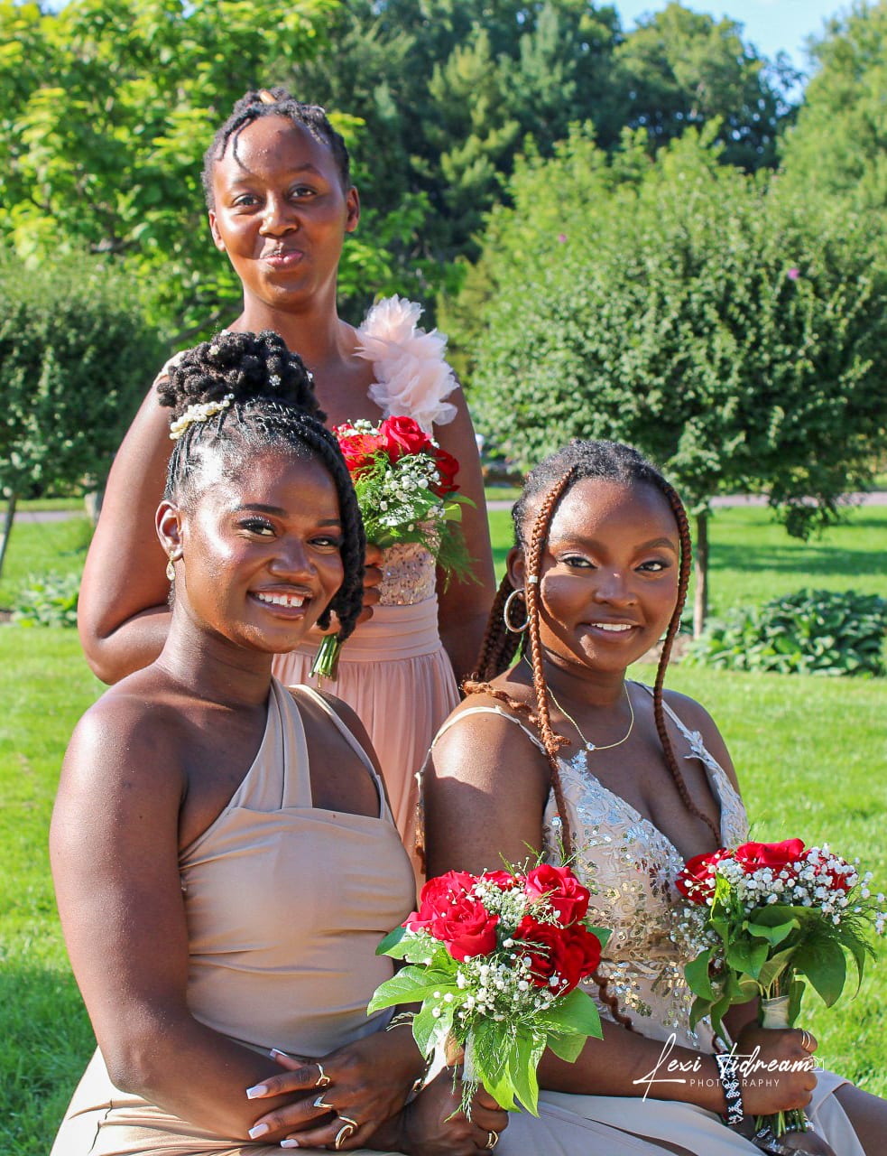 Three bridesmaids in champagne and blush dresses holding red rose bouquets