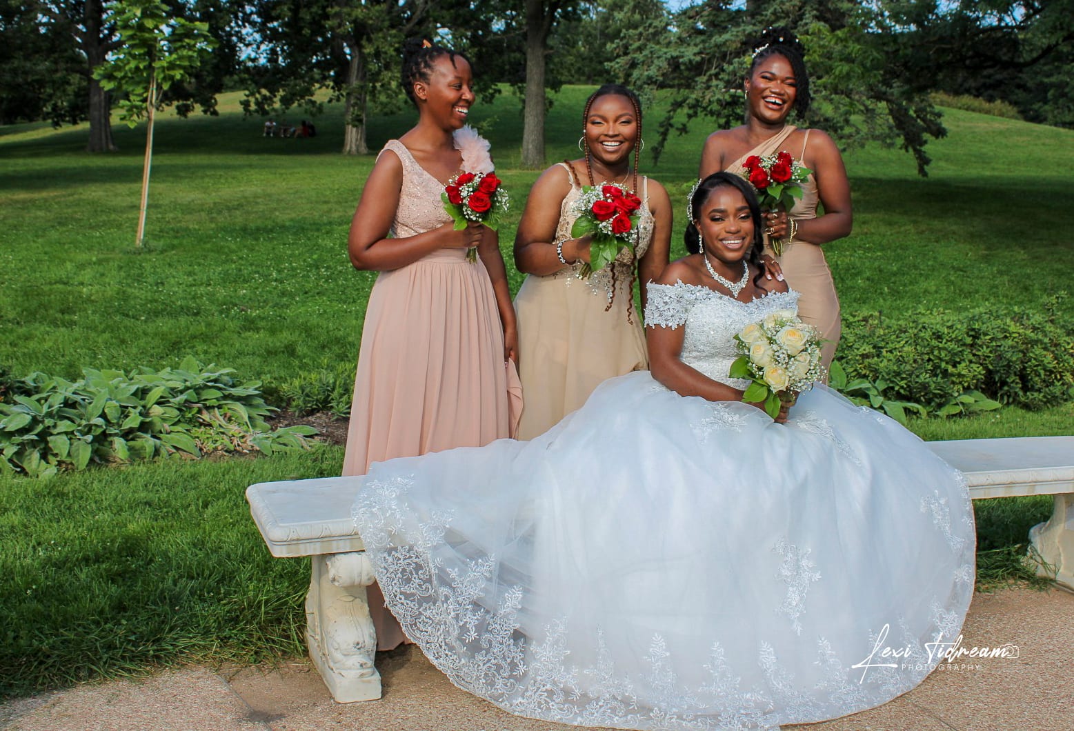 Bride seated with three bridesmaids standing behind her in a sunlit park