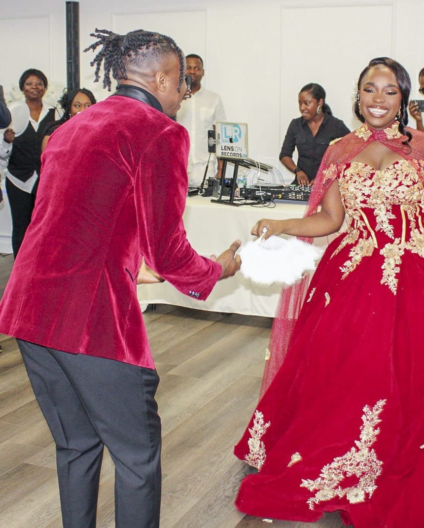A couple in red and gold on the reception floor as their guests watch and film
