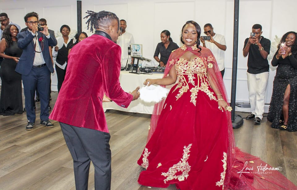 Couple dancing at a celebration, one in a red and gold gown, guests watching