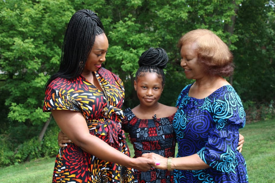 Grandmother, mother and young daughter in matching African print dresses holding hands