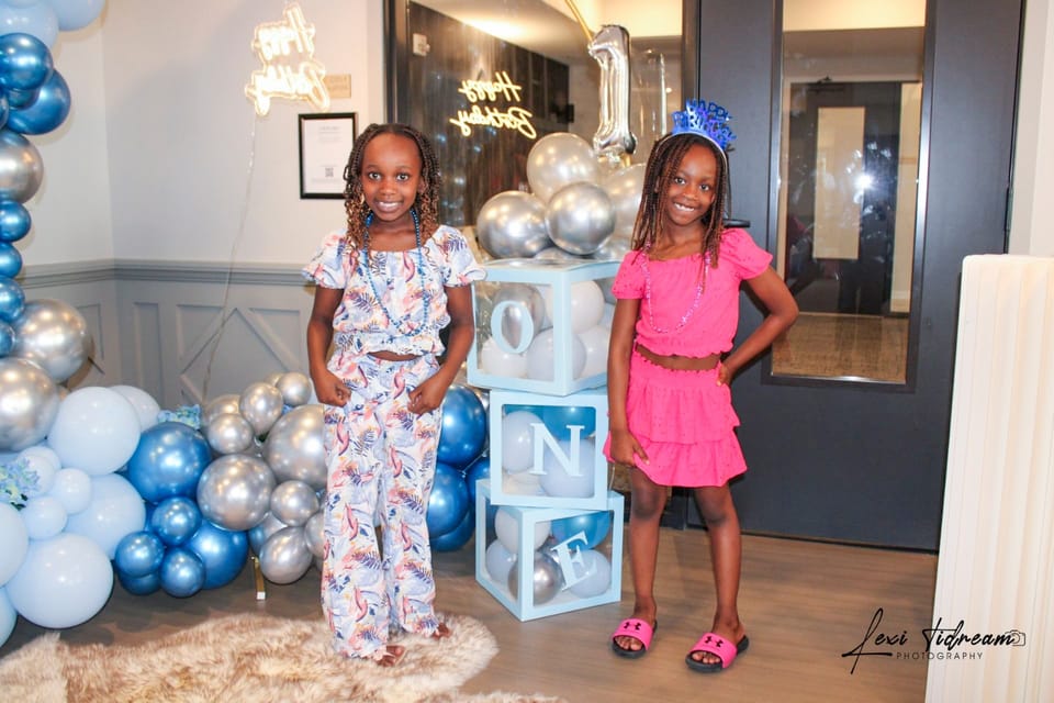Two girls posing at a birthday party decorated with blue and silver balloons