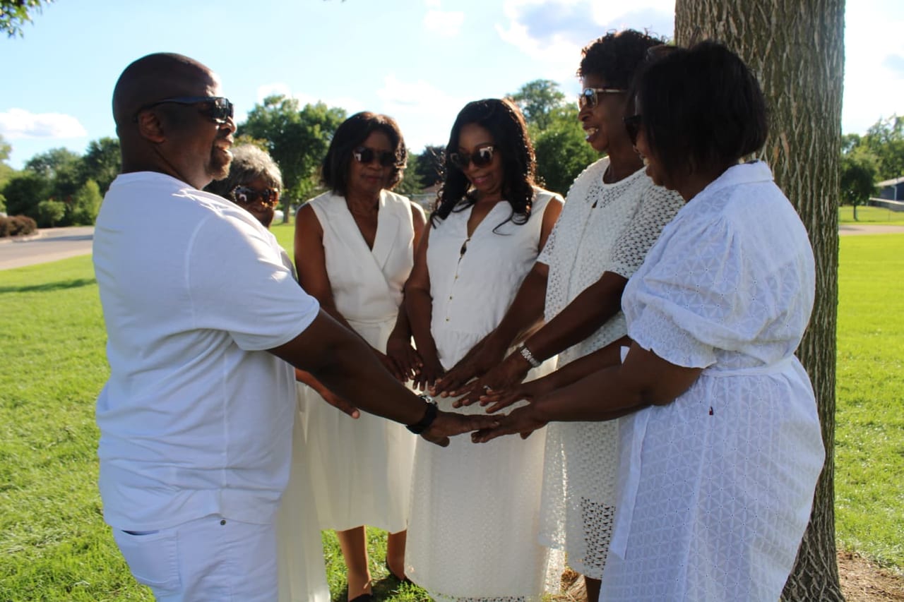 A family dressed in white joining their hands together in a circle beneath a tree