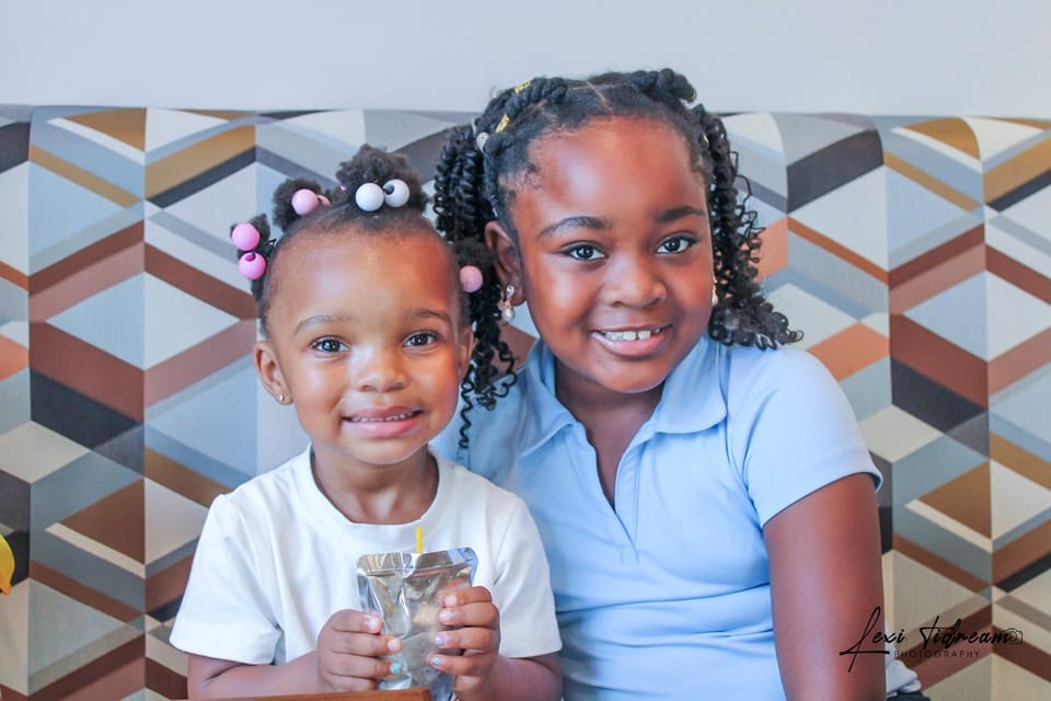 Two young sisters smiling together against a patterned studio backdrop