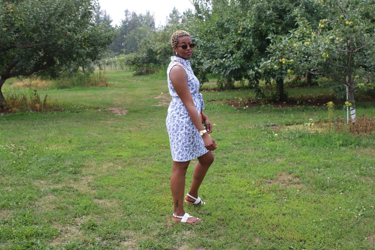 A woman in a light patterned dress walking between the rows of an apple orchard